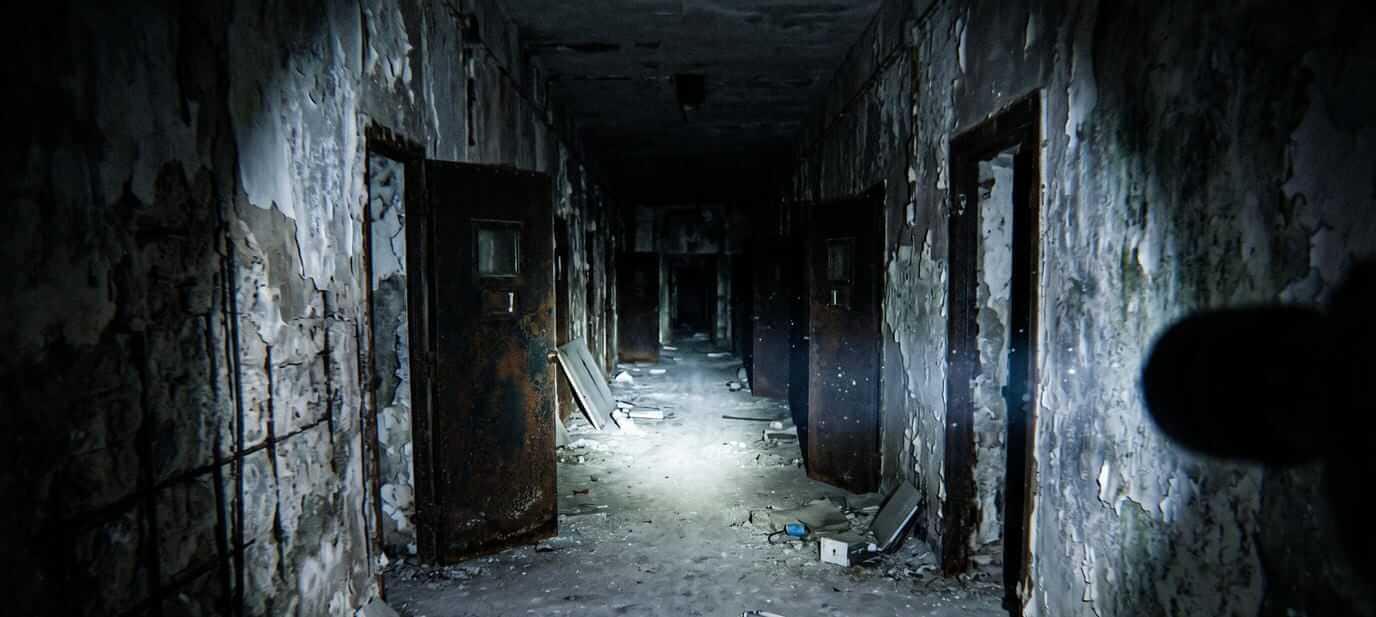 Paranormal investigators walking down a dark asylum corridor at night with flashlights